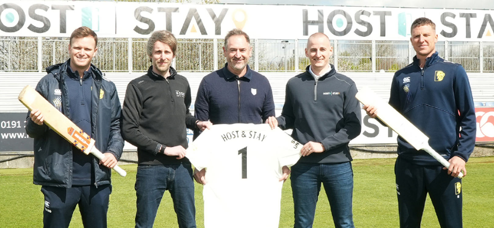 People on a cricket pitch holding a Host & Stay t-shirt