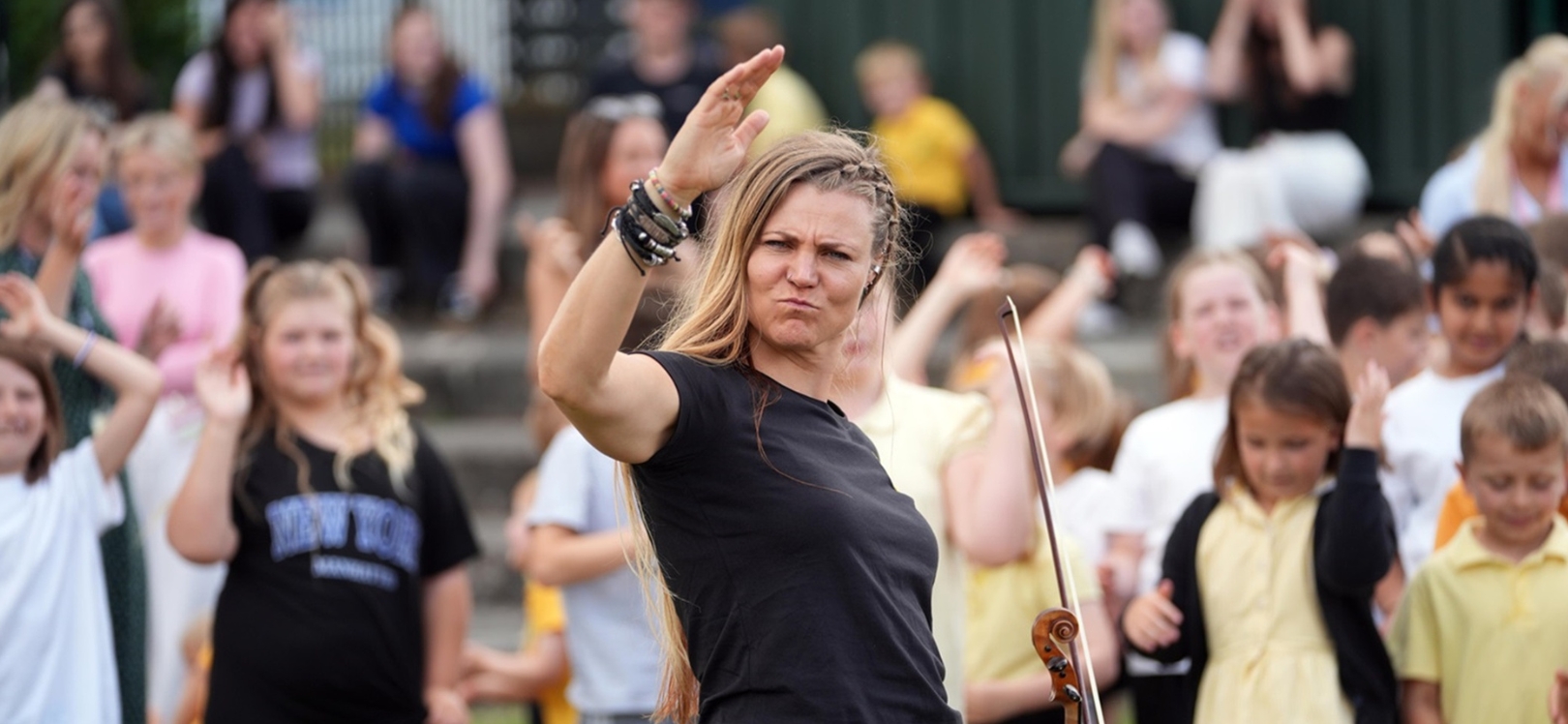 A woman holding a violin with children in the background